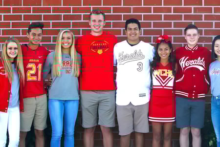 Un grupo de estudiantes de la Whittier Christian High School está frente a una pared de ladrillo rojo con diferentes camisetas deportivas y ropa de ocio.
