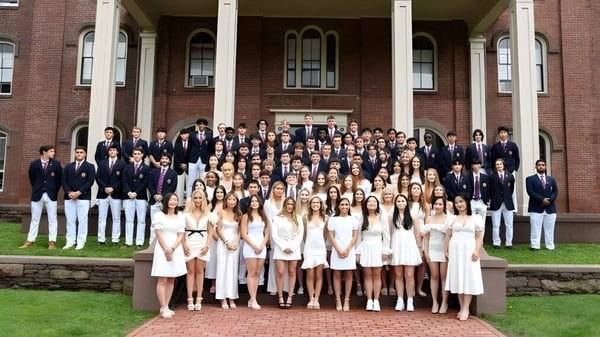 Un grupo de estudiantes está vestido con ropa formal frente al edificio histórico de la Wilbraham & Monson Academy.