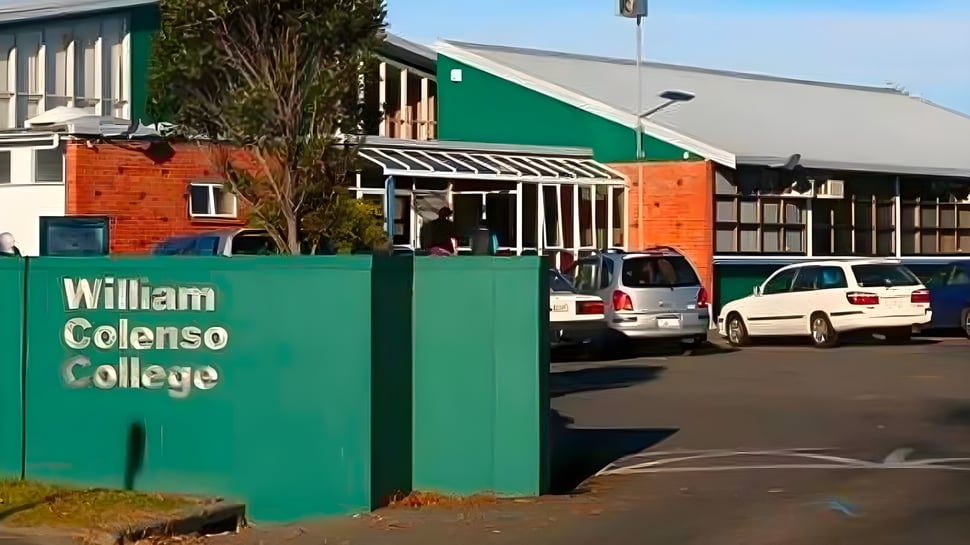 Un cartel verde con el nombre William Colenso College frente a un edificio de ladrillo y coches estacionados.