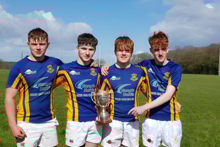 Cuatro estudiantes de la Wilson's Hospital School están en un campo de césped sosteniendo juntos un trofeo deportivo.