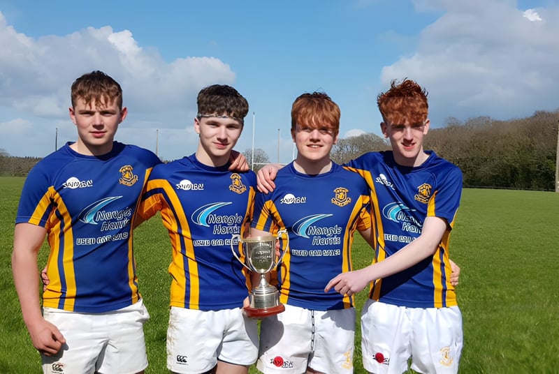 Cuatro estudiantes de la Wilson's Hospital School están en un campo de césped sosteniendo juntos un trofeo deportivo.