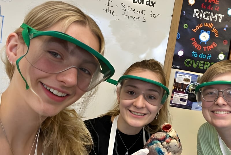 Tres estudiantes de la Winchendon School con gafas de protección están en el aula frente a una pizarra.
