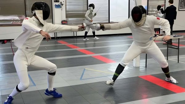 Dos estudiantes llevan ropa de esgrima y realizan un duelo en el deporte de esgrima en el terreno de Winchester College.