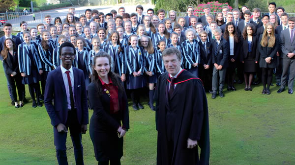 Un grupo de estudiantes de la Windermere School está en togas de graduación en un campo frente a un edificio.
