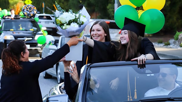 Estudiantes de la Windsor Secondary School con birretes y togas sosteniendo flores en la ceremonia de graduación.