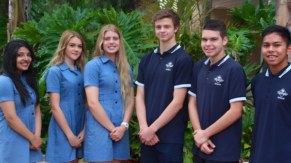 Un grupo de estudiantes está en el área exterior tropical del terreno de la Wirreanda Secondary School.