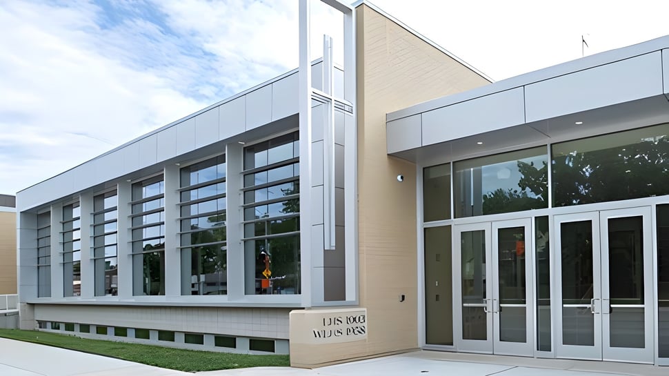 El moderno edificio de varios pisos con grandes ventanales de la Wisconsin Lutheran High School está rodeado de áreas verdes bajo un cielo nublado.