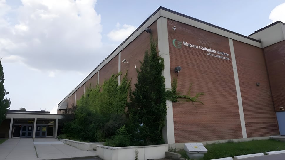 El edificio del Woburn Collegiate Institute está rodeado de vegetación verde y se ve bajo un cielo claro.