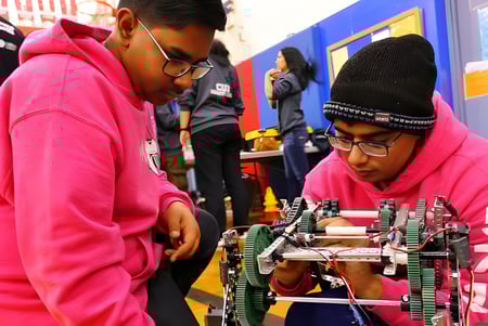 Dos estudiantes con sudaderas rosas examinan un dispositivo mecánico en el aula de tecnología del Woburn Collegiate Institute.