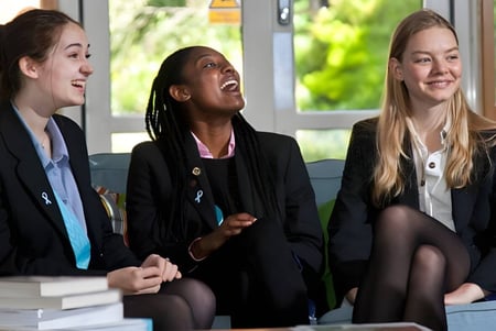 Tres alumnas de la Woldingham School están sentadas en ropa de negocios y conversan frente a una ventana luminosa.