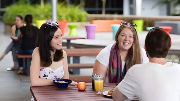 Estudiantes de la Wollongong University disfrutan juntos de una comida al aire libre frente a un fondo colorido.