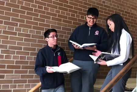 Tres estudiantes del Woodbridge College están frente a una pared de ladrillo y discuten juntos.