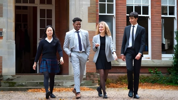 Cuatro personas bien vestidas están de pie en los escalones de un edificio de ladrillo en el campus de la Woodbridge School en otoño.