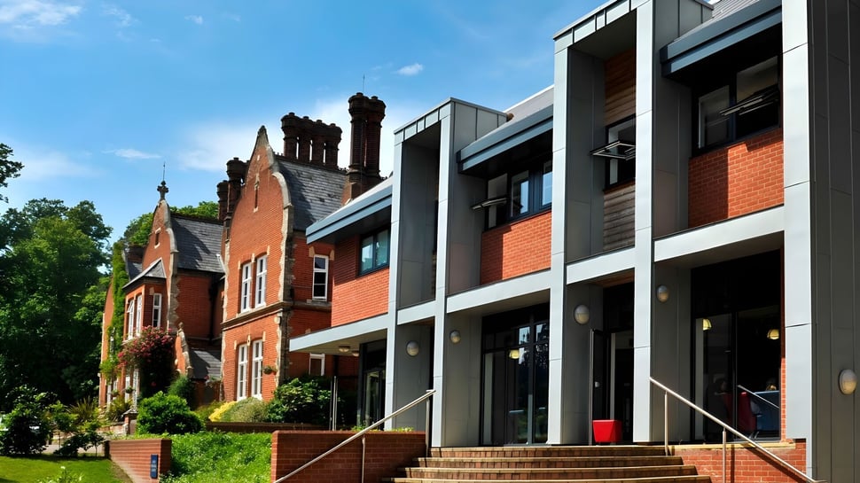 El moderno edificio de ladrillo de la Woodbridge School está rodeado de árboles verdes y se encuentra bajo un cielo azul claro.