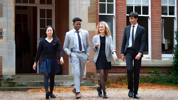 Cuatro personas bien vestidas están de pie en la escalera de un edificio de ladrillo en el campus de la Woodbridge School en otoño.