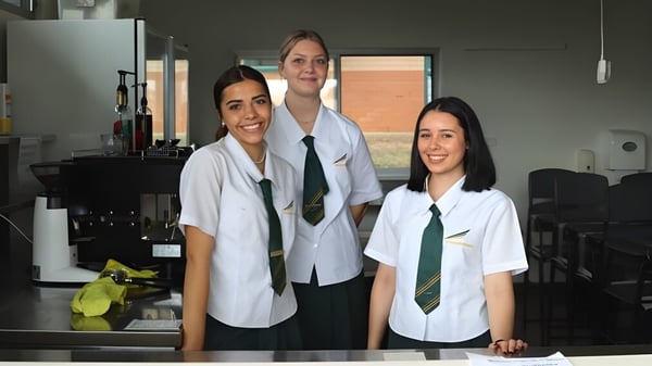 Tres estudiantes están juntas en batas blancas en un laboratorio en el campus del Woodcrest State College.