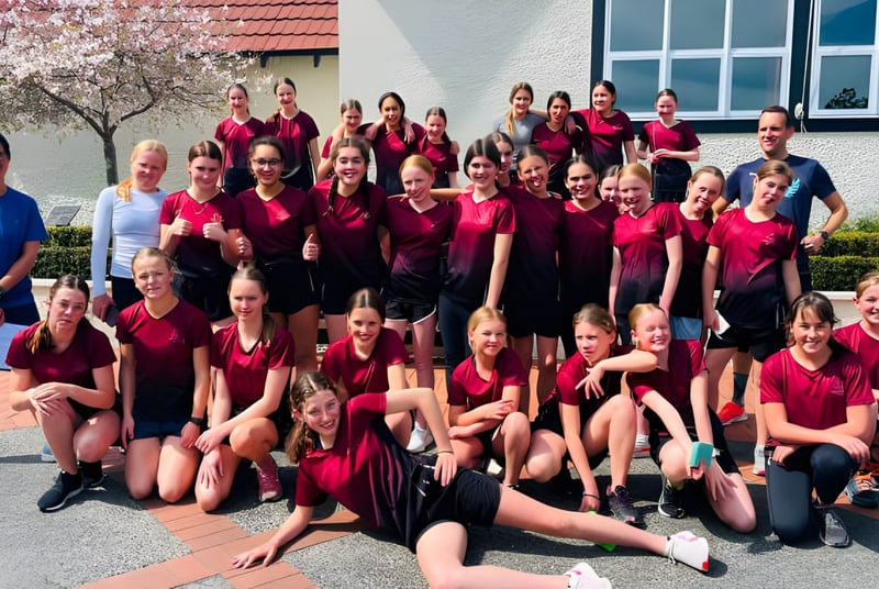 Un gran grupo de alumnas en uniformes rojos está frente a un edificio con techo de tejas rojas en el campus de Woodford House.