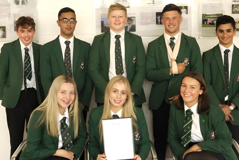 Un grupo de estudiantes de la Woodhouse Grove School en uniforme escolar verde posan en un edificio escolar frente a imágenes en la pared.