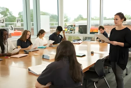 Estudiantes de la Woodward Academy trabajan juntos en una mesa en un aula con grandes ventanas.