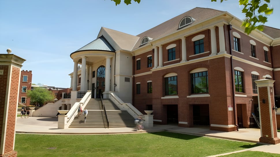 El edificio de ladrillo de la Woodward Academy con entrada de columnas y grandes ventanas se encuentra en una zona de césped con árboles.
