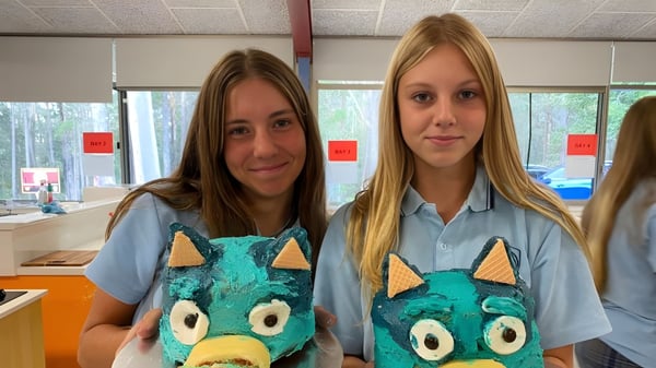 Dos estudiantes de la Woolgoolga High School llevan camisetas uniformes con diseño de monstruo y están en un aula.