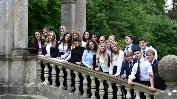 Un grupo de estudiantes está en el balcón de Worksop College rodeado de vegetación verde y columnas de piedra.