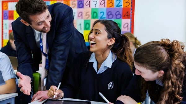 Un grupo de estudiantes de la Wycombe Abbey School discute con su profesora en el aula frente a coloridos carteles de aprendizaje.