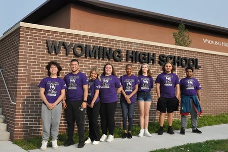 Un grupo de estudiantes está frente al edificio de la Wyoming High School con el nombre de la escuela en la fachada.