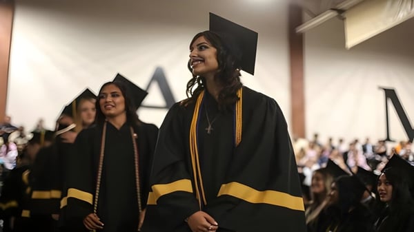Los graduados de la Xavier College Preparatory High School llevan togas negras y están de pie en un pasillo con personas al fondo.