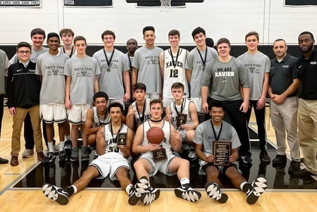 Un grupo de jugadoras y jugadores de baloncesto de la Xavier High School posan con trofeos en la cancha de baloncesto.