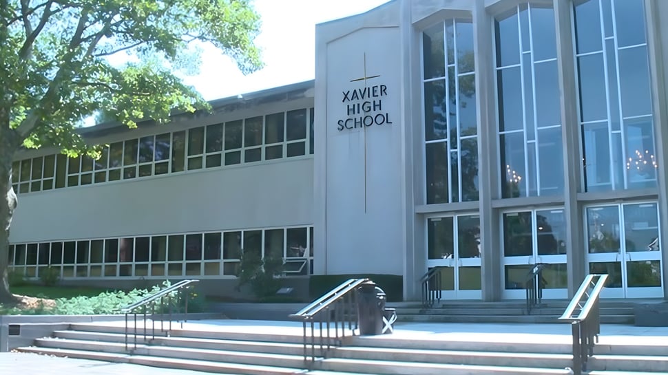 Se puede ver el edificio escolar de la Xavier High School con grandes ventanas y una entrada rodeada de áreas verdes.