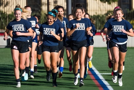 Un grupo de jóvenes jugadoras de la Xavier College Preparatory High School corre juntas en el campo de fútbol.