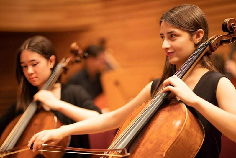 Una estudiante de la Yehudi Menuhin School toca el violonchelo en el escenario con otro músico al fondo.